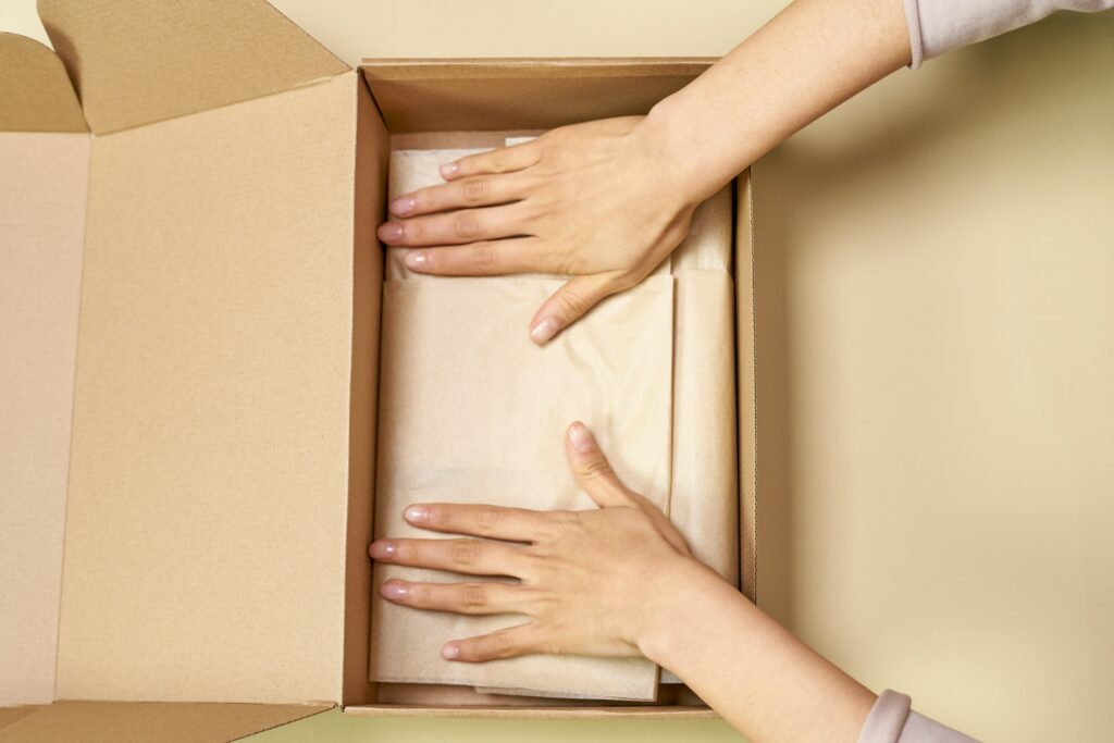 Open carton and tissue paper with two hands closing the paper